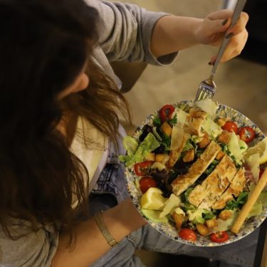 Overhead view of a woman eating a chicken salad balancing health with deliciousness.
